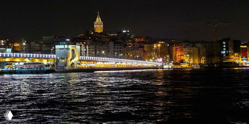 Ночной вид на набережную Стамбула и далёкую Галатскую башню, огни города отражаются в воде пролива Золотой Рог, атмосферная панорама.