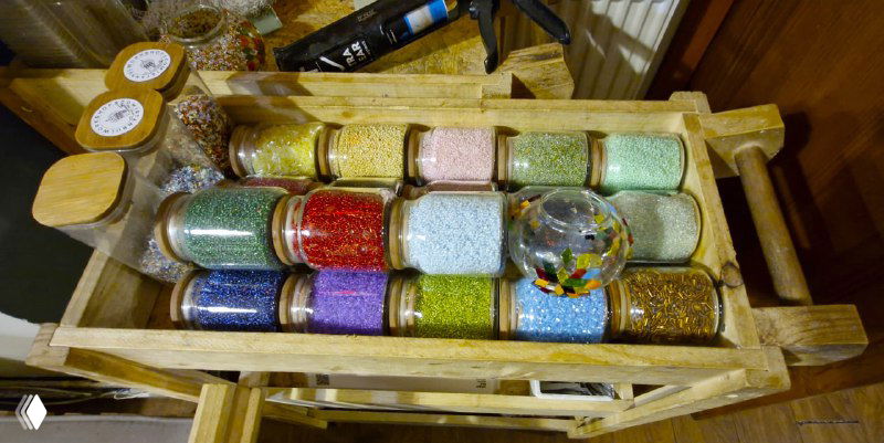 Коробочка с бисером и мелкими стеклянными бусинами разных оттенков и текстур, используемыми для заполнения пространства между мозаичными кусочками.