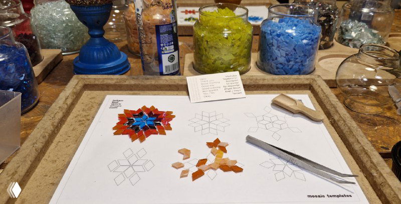 Лист с шаблоном узора и выложенные кусочки стекла: красные и оранжевые фрагменты формируют начальный рисунок для мозаичной лампы.