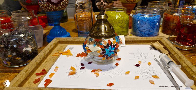 Частично собранная мозаичная лампа на рабочем месте: приклеенные стеклышки и заполнение бисером видны в процессе сборки изделия.