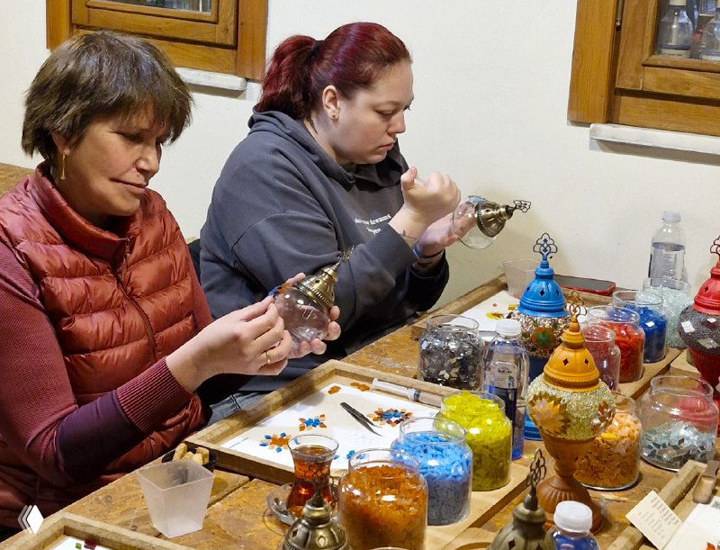 Две участницы мастер-класса аккуратно выкладывают и приклеивают элементы мозаики на стеклянную основу, сосредоточенная работа руками.