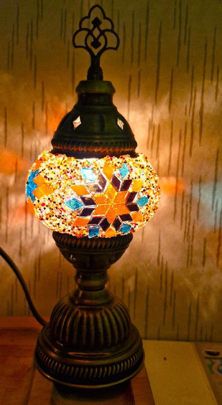 Включённая мозаичная лампа, её стекляшки просвечивают тёплым светом, на стене отражается тот же орнамент разноцветных бликов.