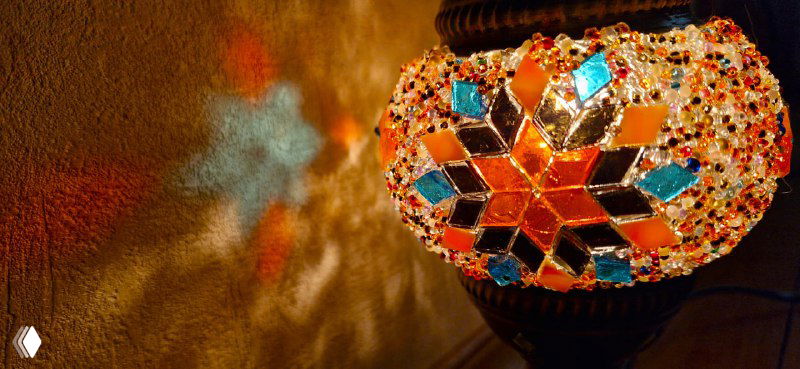 Крупный план готовой мозаичной лампы: детальный вид звёздчатого узора из цветного стекла и эффектных бликов на поверхности изделия.