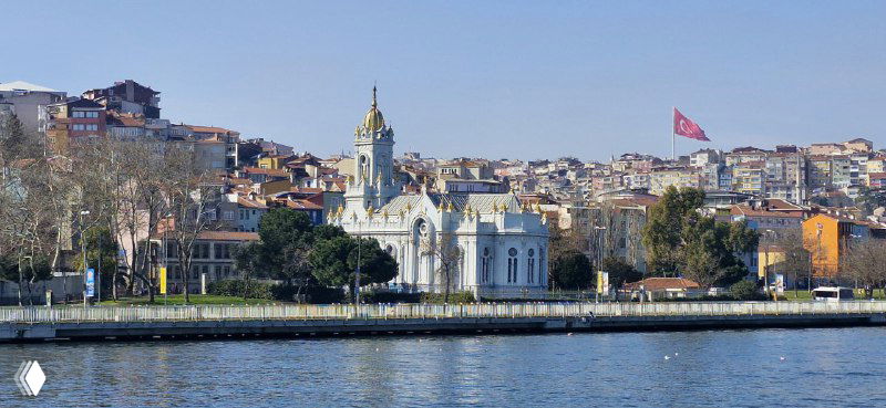 Болгарская церковь Святого Стефана у воды на фоне жилых кварталов и флагов на холме по другую сторону бухты