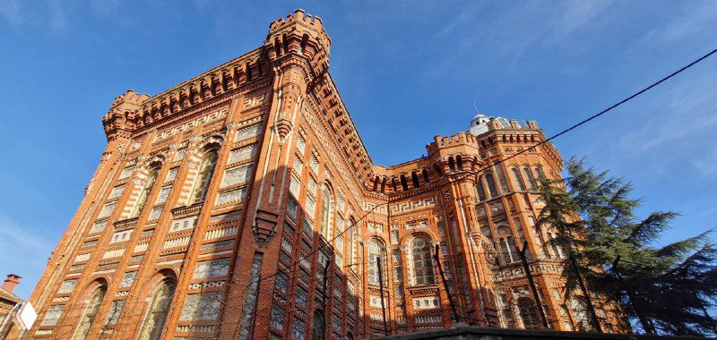 Монументальное здание из красного кирпича на холме — греческий православный лицей, вид с близкого расстояния под голубым небом