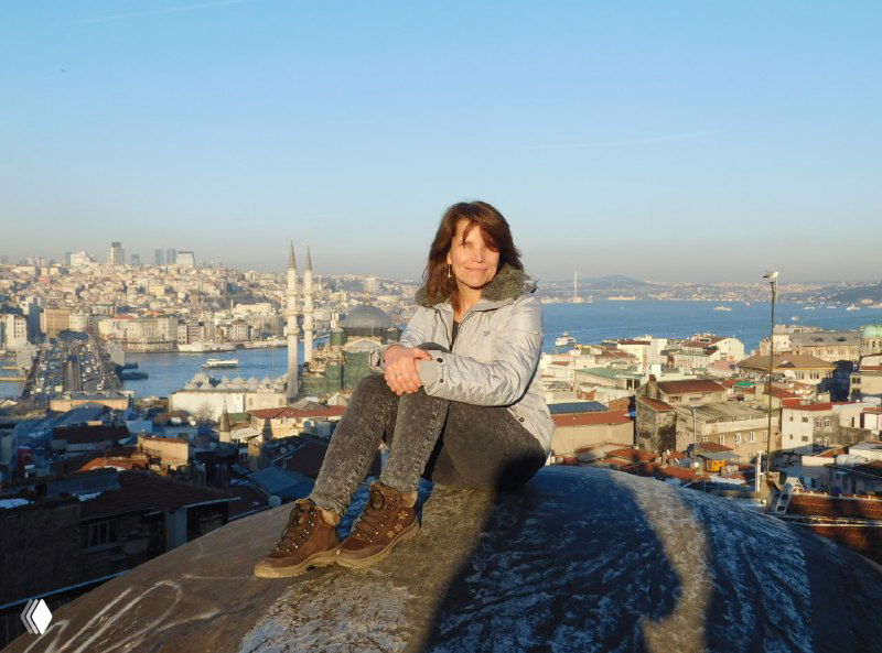 Автор сидит на куполе крыши с видом на Стамбул: человеческая фигура на переднем плане и городской пейзаж с Галатой и морем на заднем.