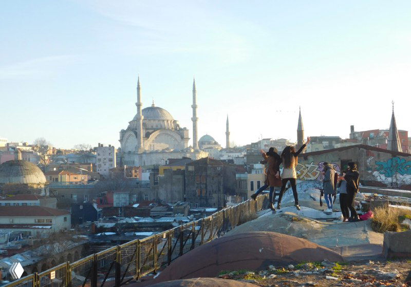 Несколько людей на куполе-крыше любуются заходящим солнцем и панорамой Стамбула — кадр отражает атмосферу наблюдения и городской романтики.