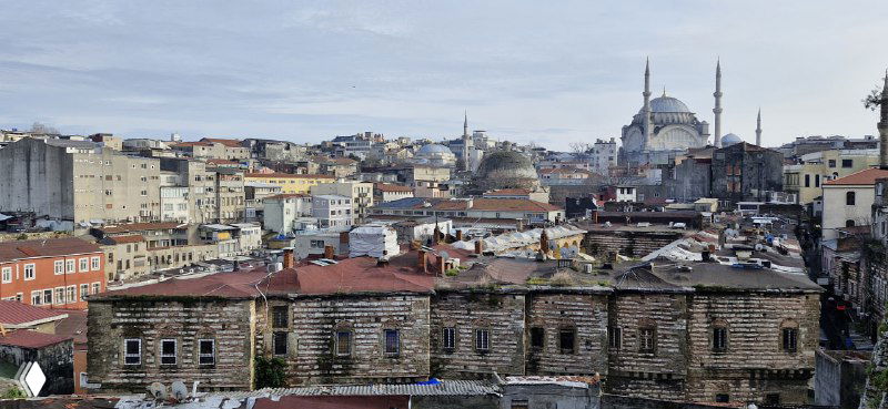 Длинный панорамный вид на плотную застройку и крыши старого города Стамбула, видны купола мечетей и разноуровневые дома вдоль горизонта.