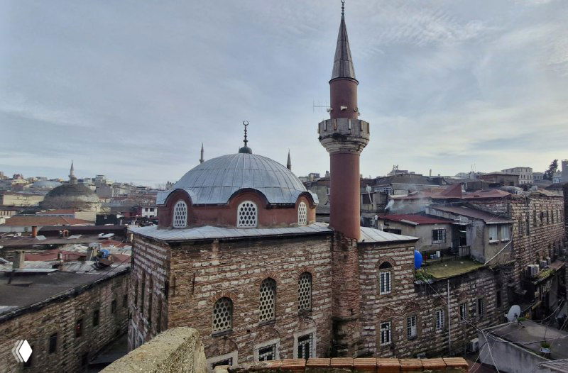 Крыша с небольшим минаретом вблизи и окружающие старые здания, вид с высоты подчеркивает каменную архитектуру и плотность исторических построек.