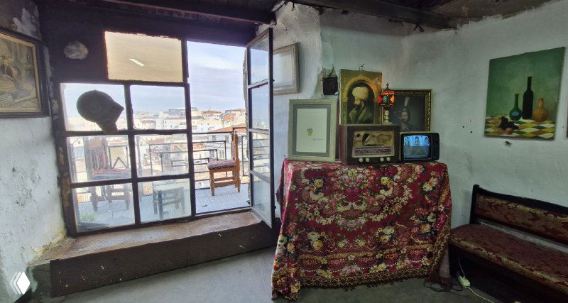 Небольшое помещение в Валиде Хан с окном, старой мебелью и видом на внешний городской пейзаж — интерьер мастерской или лавки, простой быт.