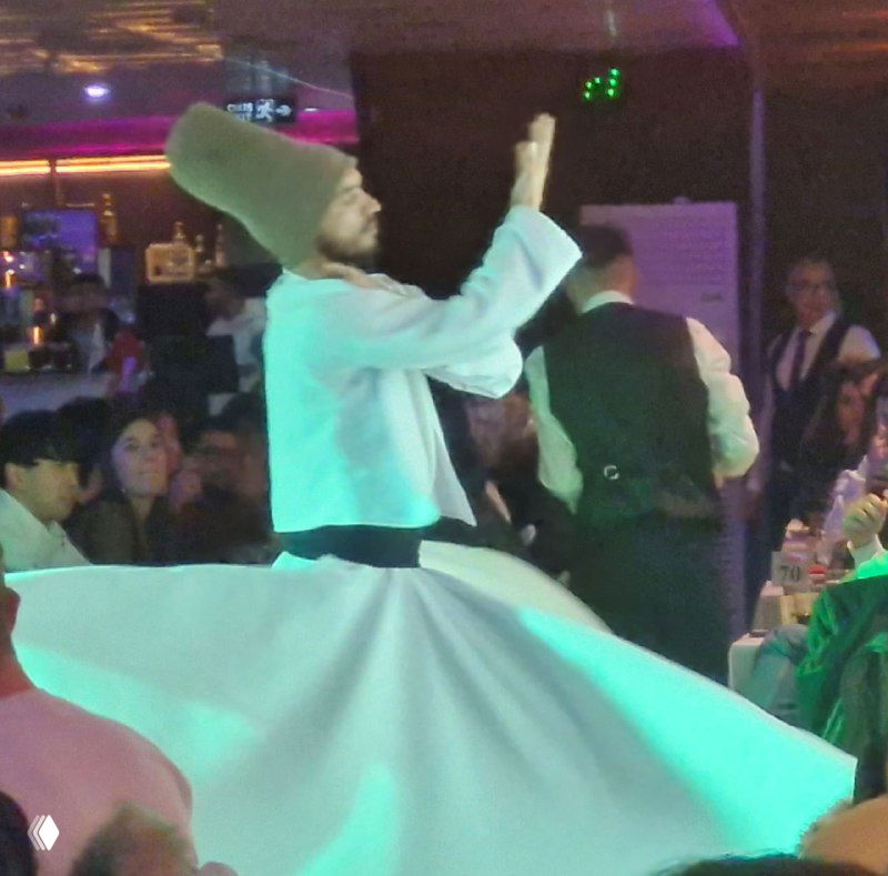 Внутренний кадр с борта корабля: танец вращающегося дервиша в длинной белой юбке, публика за столиками и сцена в тёплом свете.