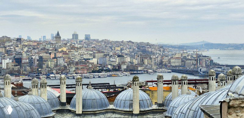 Купола и малые башенки на фоне плотной застройки Стамбула; вид с высоты подчёркивает архитектуру и морской горизонт.