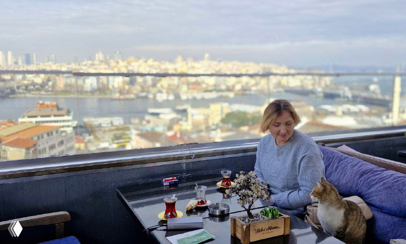 Открытая терраса кафе с гостем и собакой, на фоне размытый вид на Босфор и городской берег — атмосфера отдыха на высоте.