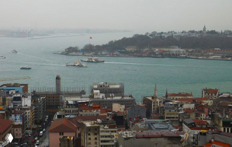 Панорама порта и Босфора с причалами и флагом на берегу; кадр показывает морскую часть города и промышленный берег.