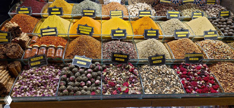Стеллажи с кучами специй и сухофруктов: цветные горки приправ, яркий ассортимент пряностей и сушёных плодов на прилавке рынка специй.