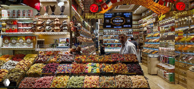 Прилавок с разнообразными орехами, сухофруктами и упаковками чаев: плотный ассортимент, множество банок и мешков приманивают покупателей на базаре.