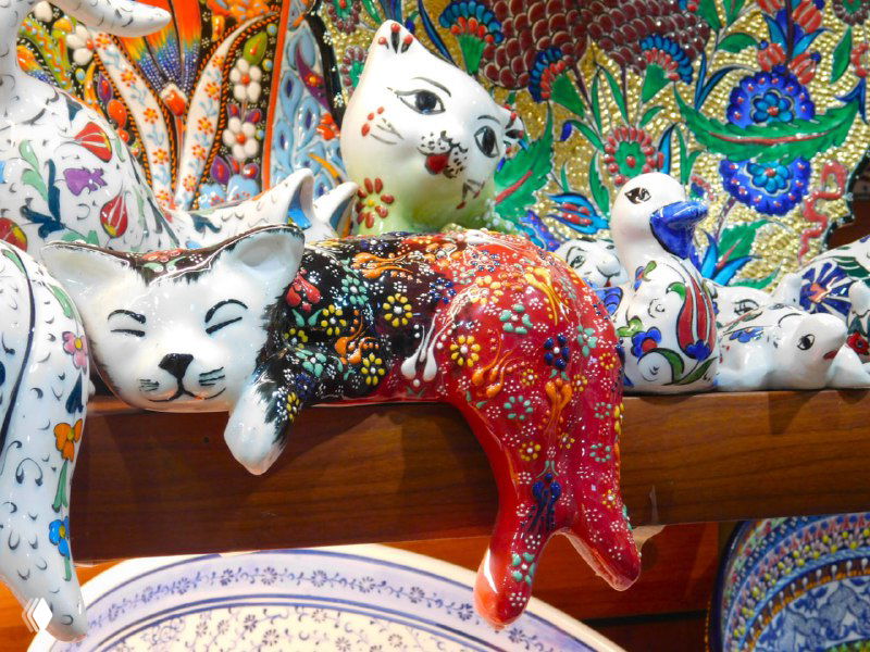 Фарфоровые фигурки и расписные статуэтки в витрине: цветные декоративные изделия, часто покупаемые как необычные сувениры с базара.