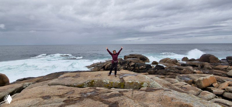 Человек на морских скалах, раскинутые руки и открытое океанское пространство — момент радости и свободы на конечных этапах пути.