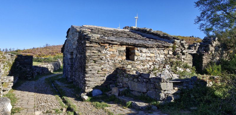 Старинное каменное убежище в горной местности вдоль Камино: низкое строение с каменной крышей и зелёными пастбищами вокруг, тихая панорама.