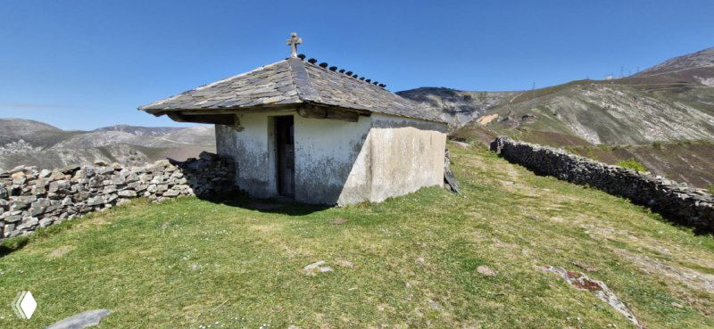 Небольшая часовня или хижина на холме вдоль маршрута Камино, окружённая каменными оградами и горными ландшафтами под ясным небом.