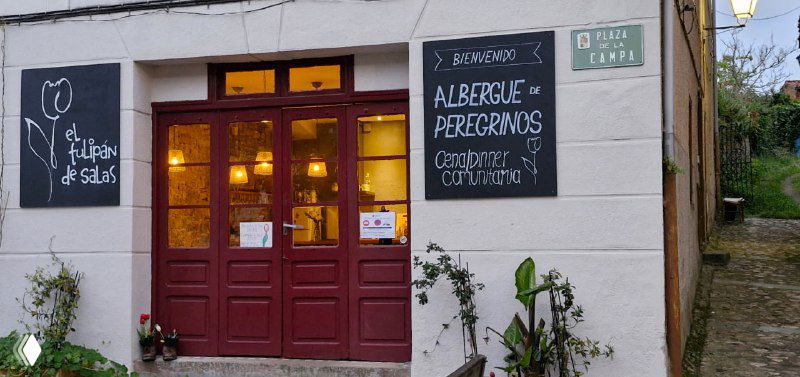 Фасад уютного частного альберге с входной дверью и вывеской "albergue"; вечернее освещение создаёт тёплую атмосферу гостеприимства.