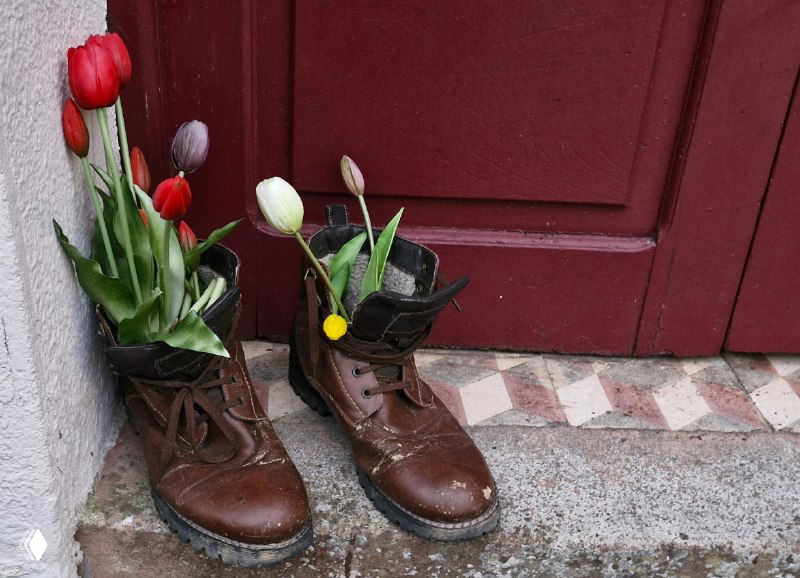 Необычная уличная композиция: старые ботинки, наполненные тюльпанами у порога альберге — уютная деталь оформления входа.
