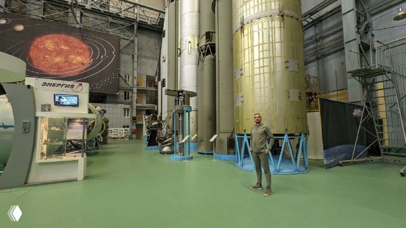 Интерьер музейного зала Роскосмоса с крупной техникой и турбинами, человек на фоне для масштаба — атмосфера экспозиции космической отрасли.