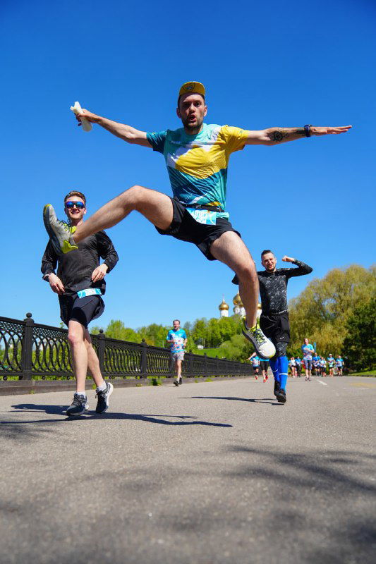 Группа участников забега прыгает и веселится на трассе у набережной в Ярославле; яркое голубое небо и позитивная атмосфера мероприятия.