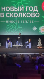 Зрительный зал и сцена с баннером «Новый год в Сколково», на сцене видны спикеры и зрители в затемнённом пространстве аудитории.