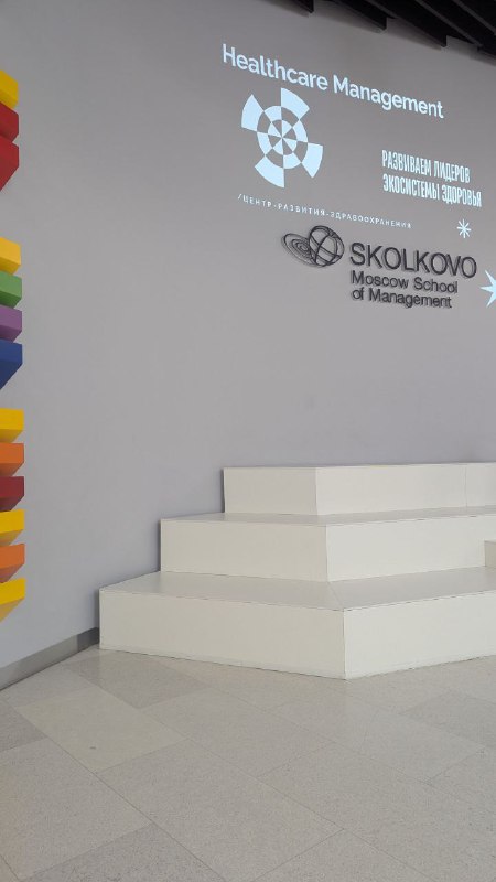 Интерьер Школы управления СКОЛКОВО: белая сцена, проекционная стена с логотипом и ступени — кадр из пространства мероприятия.