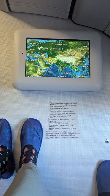 Вид с лавки в самолете на экран с маршрутом и ногах пассажира, кадр передает момент перелета и небольшую усталость путешественника в дороге.