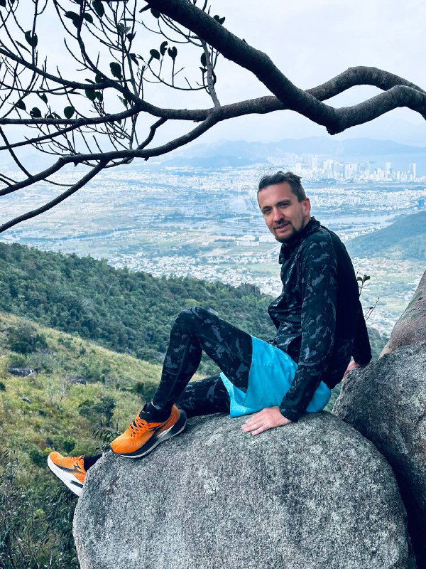 Автор отдыхает на большом камне с видом на город и побережье внизу, кадр демонстрирует сочетание природы и городской панорамы за спиной.