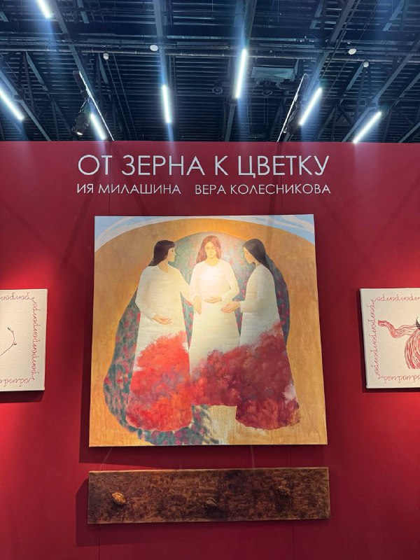 Красная экспозиционная панель с крупной картиной и надписью названия проекта, видно оформление стенда с центровой работой.