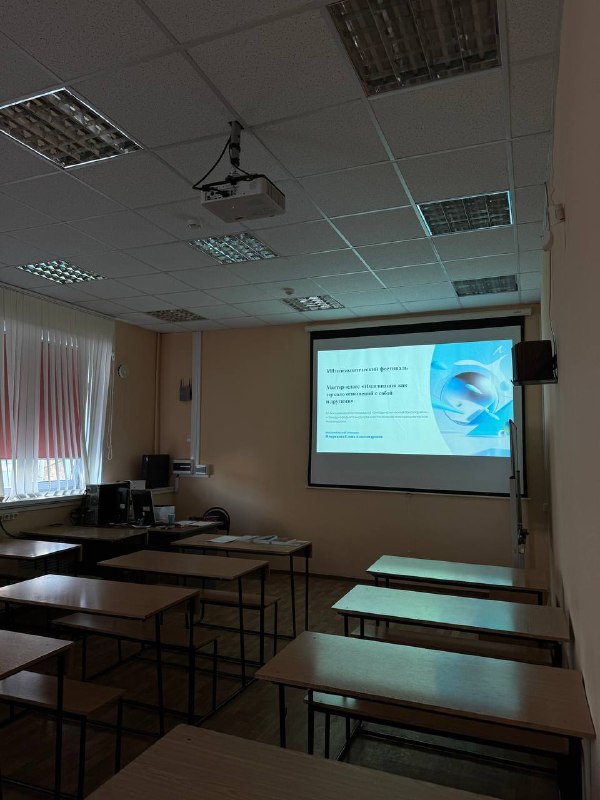 Аудитория с пустыми партами и экраном, на котором виден слайд выступления: учебная и конференционная обстановка внутри института.
