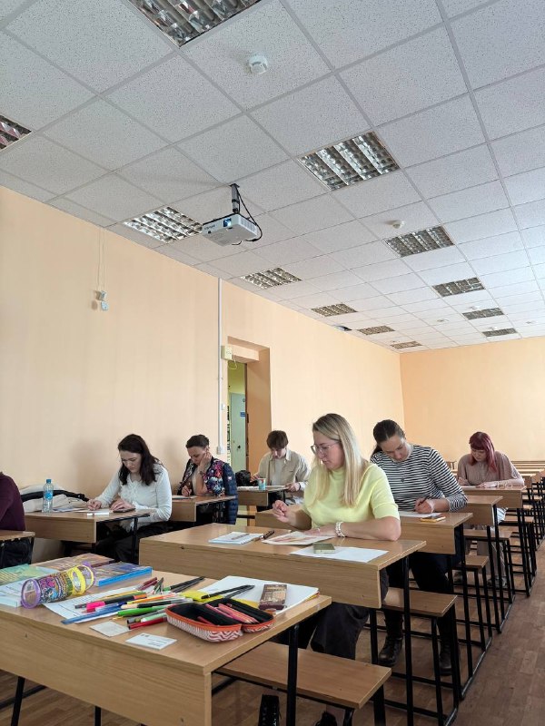 Группа участников в аудитории за партами: люди записывают и слушают, автор в жёлтом ведёт занятие — тёплая и сосредоточенная атмосферa встречи.