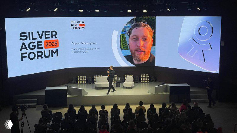 Панорамный вид сцены Silver Age Forum с логотипом мероприятия и несколькими докладчиками на фоне большого экрана и зрительным залом внизу.
