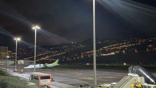Ночной вид на взлётно-посадочную полосу аэропорта Мадейра: огни полосы, городской пейзаж внизу и стоящие в ожидании самолёты.