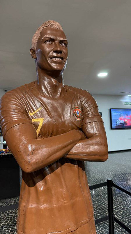 Фигура спортсмена, выполненная из шоколада или бронзы, на постаменте в зале музея; музейное ограждение и освещение видны вокруг.