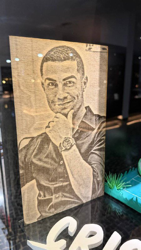 Гравюра или творческая работа с портретом спортсмена в витрине музея; видны блики на стекле и окружающие предметы коллекции.