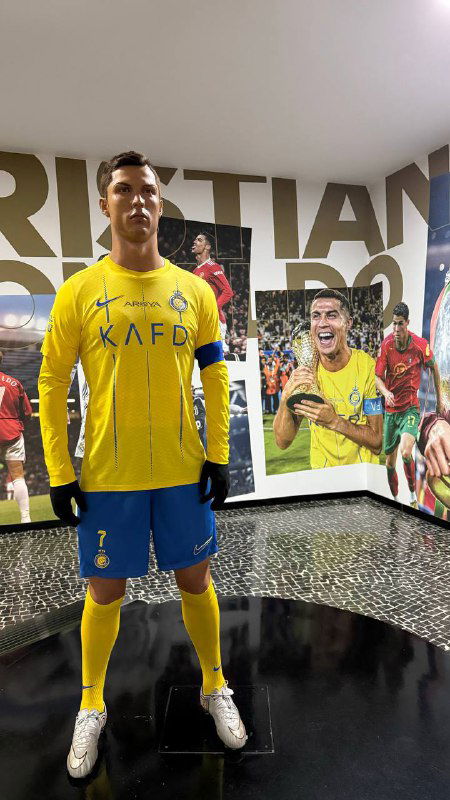 Ростовая фигура в спортивной форме внутри музея на фоне настенной графики и плакатов с изображениями из карьеры футболиста.