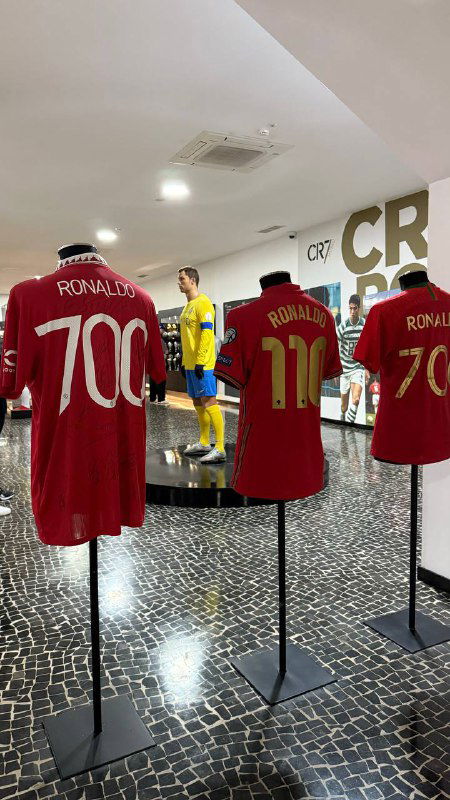 Ряд экспонатов с футбольными футболками и номерами на манекенах внутри экспозиции музея; общий план зала и экспозиционного освещения.