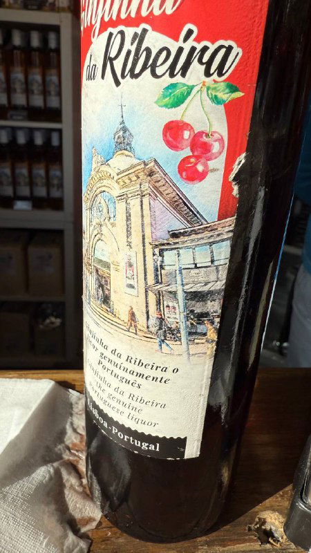 Бутылка вишнёвого ликёра с этикеткой с рисунком улицы и вишнями на деревянной поверхности — крупный план местного напитка жижинью.