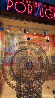 Яркая неоновая вывеска 'PORTUGAL' над витриной магазина с декоративным колесом и подсветкой — ночной городской кадр витрины.