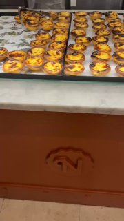 Витрина кондитерской, заполненная рядом свежих пастéis de nata: множество пирожков на прилавке, готовых к продаже.