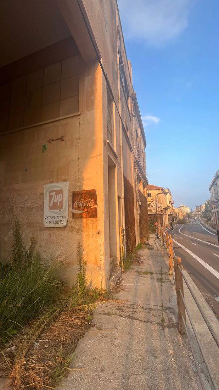 Пустынная улица с обветшалыми домами и вывесками, характерный кадр заброшенной прибрежной части города с трещинами и пустыми витринами.