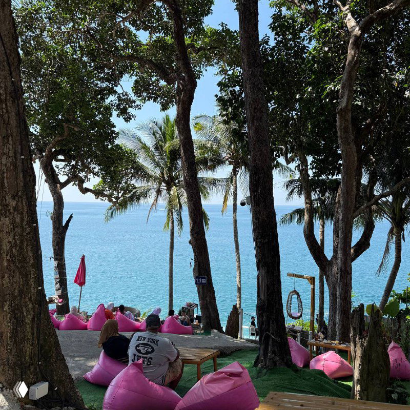 Каменистый берег с панорамным видом на море, разноцветные пуфы и качели над водой — фотозона у Viewpoint Phuket с посетителями на фоне.