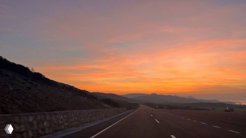 Долгая дорога на фоне яркого заката: пустынное шоссе, низкое солнце и оранжево-розовое небо — настроение вечерней поездки по острову.