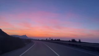 Размытый кадр закатной дороги с извилистым полотном и розово-фиолетовым небом — ощущение движения и скоростной ночной дороги через остров.