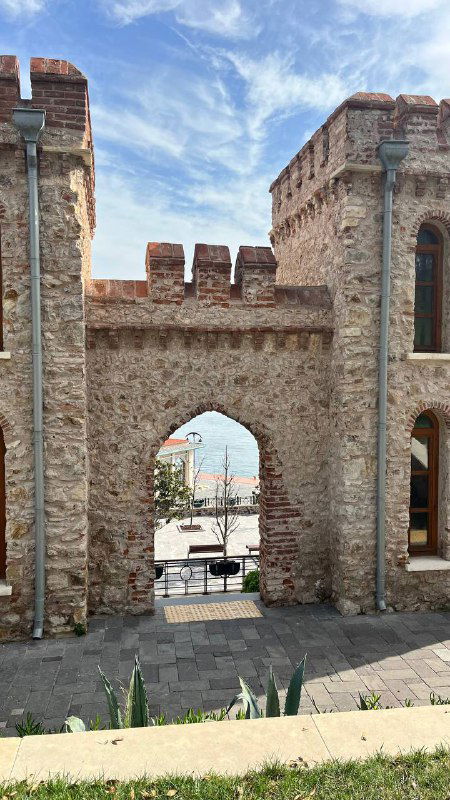 Каменная арка и фрагмент крепостной стены на острове Яссыада; вид на море сквозь проход, ясное небо и детали архитектуры.