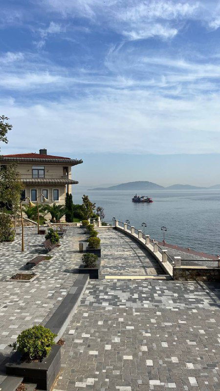 Панорамная набережная острова с прогулочной зоной, домиками и видом на море вдали; мощёная дорожка и спокойная атмосфера.